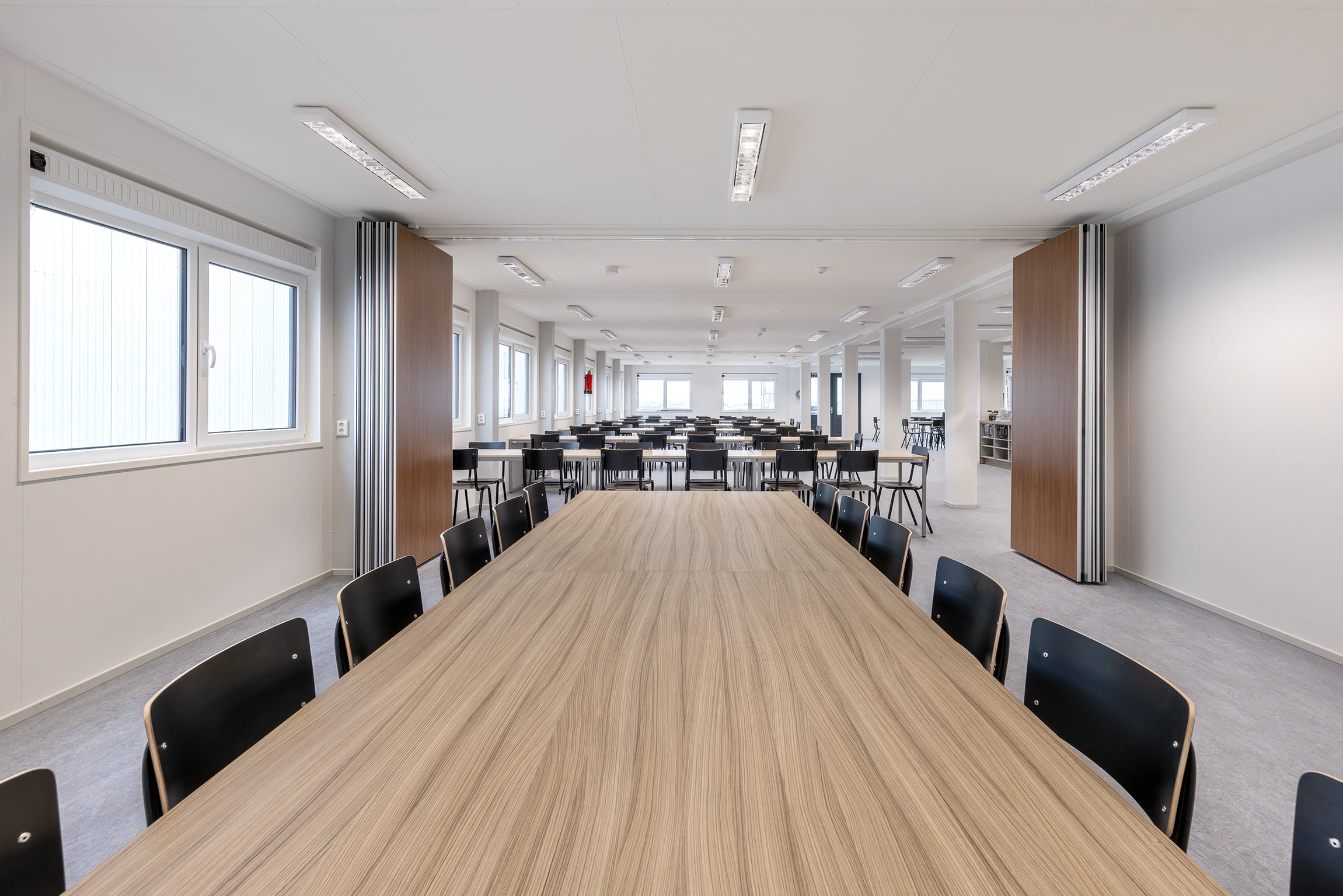 Interieur kantoorruimte: lichte modulaire kantoorruimte met lange vergadertafel en stoelen en inklapbare wanden voor extra ruimte.